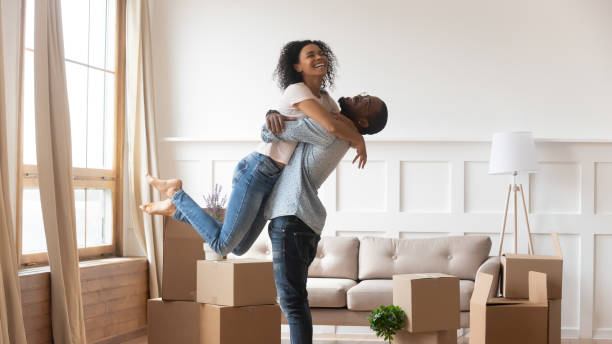 Een blij stel viert de oplevering van hun woning tussen de verhuisdozen in een lichte woonkamer