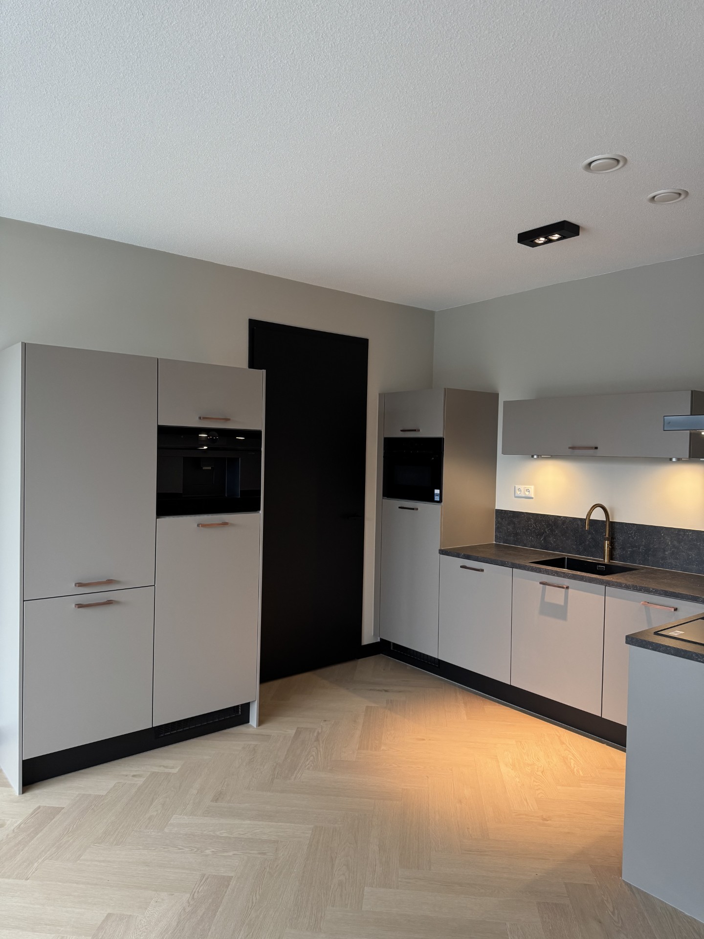 Keuken met grijze kasten, zwart werkblad en gouden kraan in Hyde Park